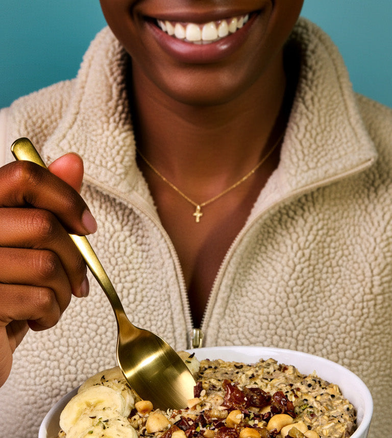 Person holding a bowl of granola with a banana and a gold spoon, against a blue background