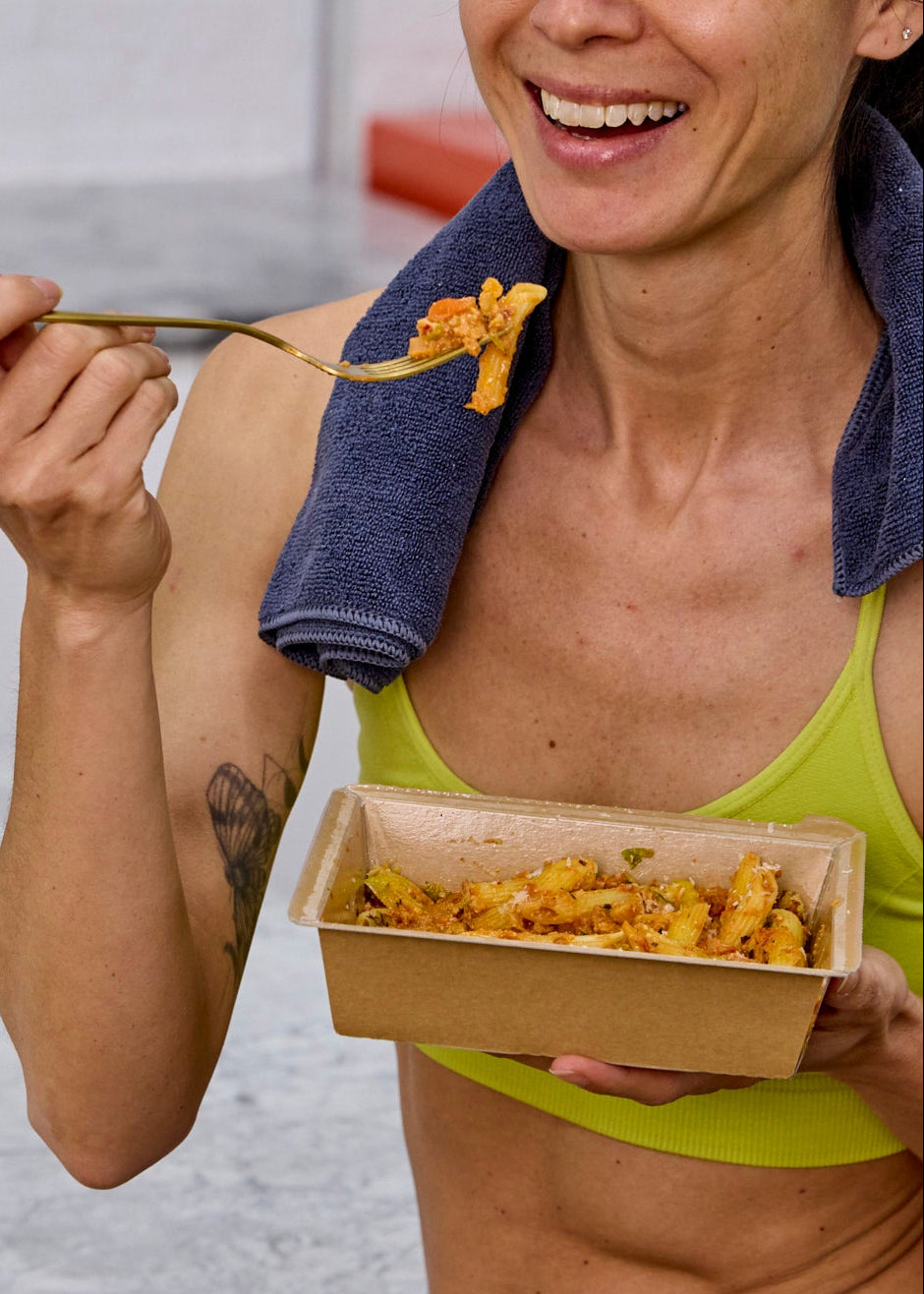 Person eating from a box with a towel over their shoulder, sitting on a bench.