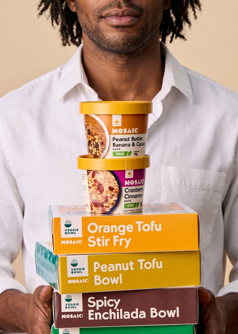 Person holding a stack of Mosaic Food food product containers against a beige background