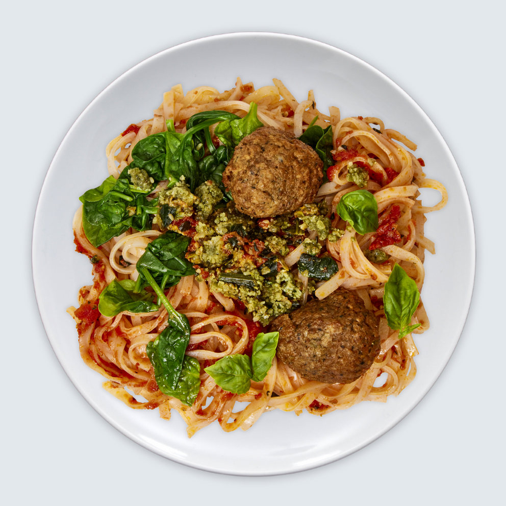 Plate of spaghetti with meatballs and greens on a white background