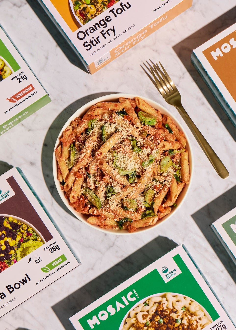 Mosaic Foods meal packaging with a bowl of pasta and a fork on a marble surface.