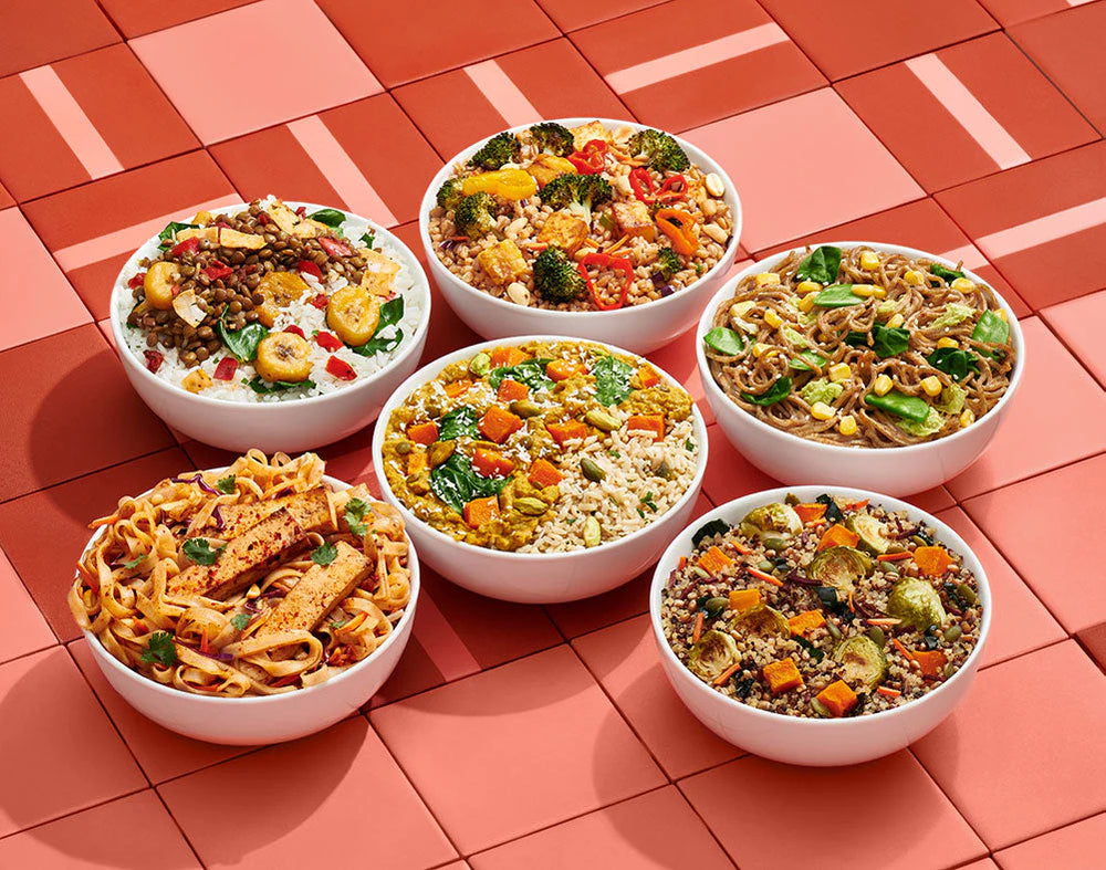 Six bowls of different types of pasta with vegetables on a red tiled background